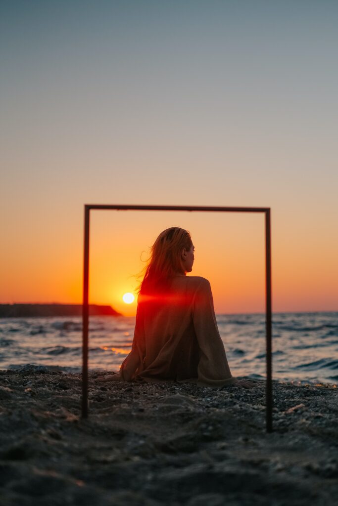 Bilden visar en person som sitter vid en strand i en solnedgång. Plastik operationer ochsom näsplastik Stockholm och Uppsala med en erfaren plastikkirurg i Uppsala.