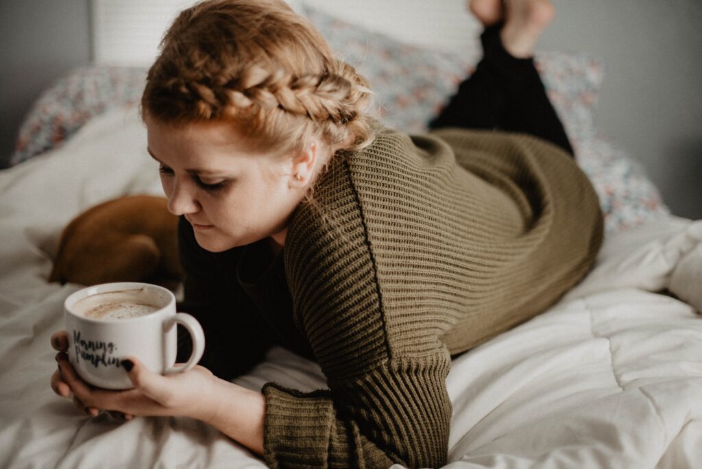 Bilden visar en person med en kaffekopp i sängen. Frukostbrickor är praktiska för att njuta av frukost på sängen.