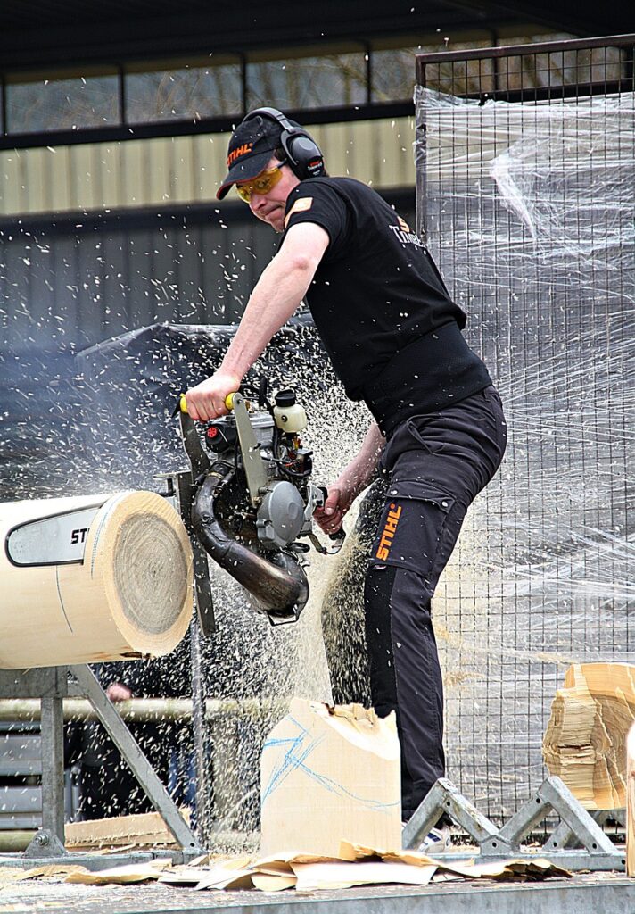 Bilden visar en person som sågar ved med motorsåg. En vedklyv klyver veden på ett effektivt sätt.